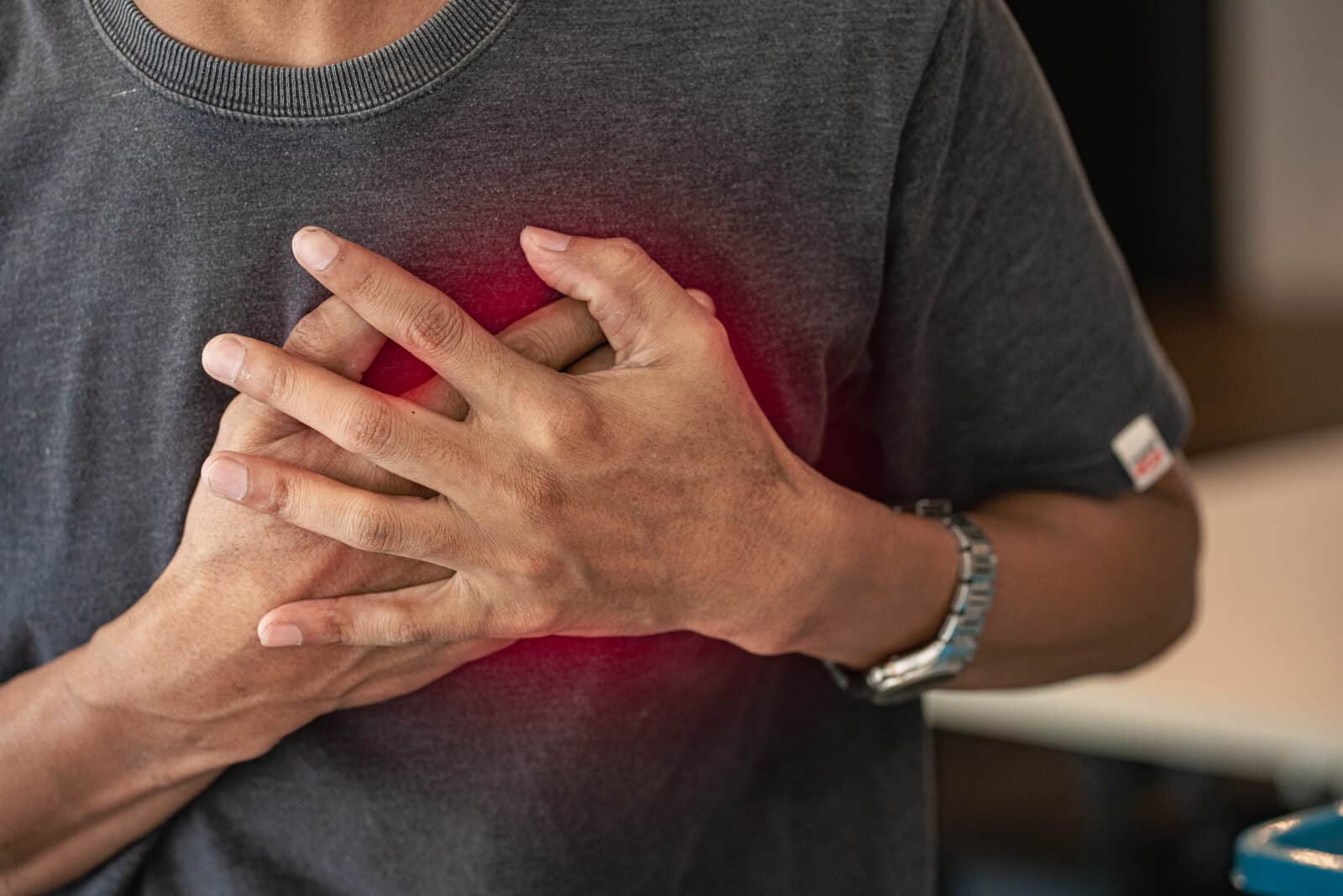 Upper torso of a person pressing their hands to their chest, suggesting chest pain.