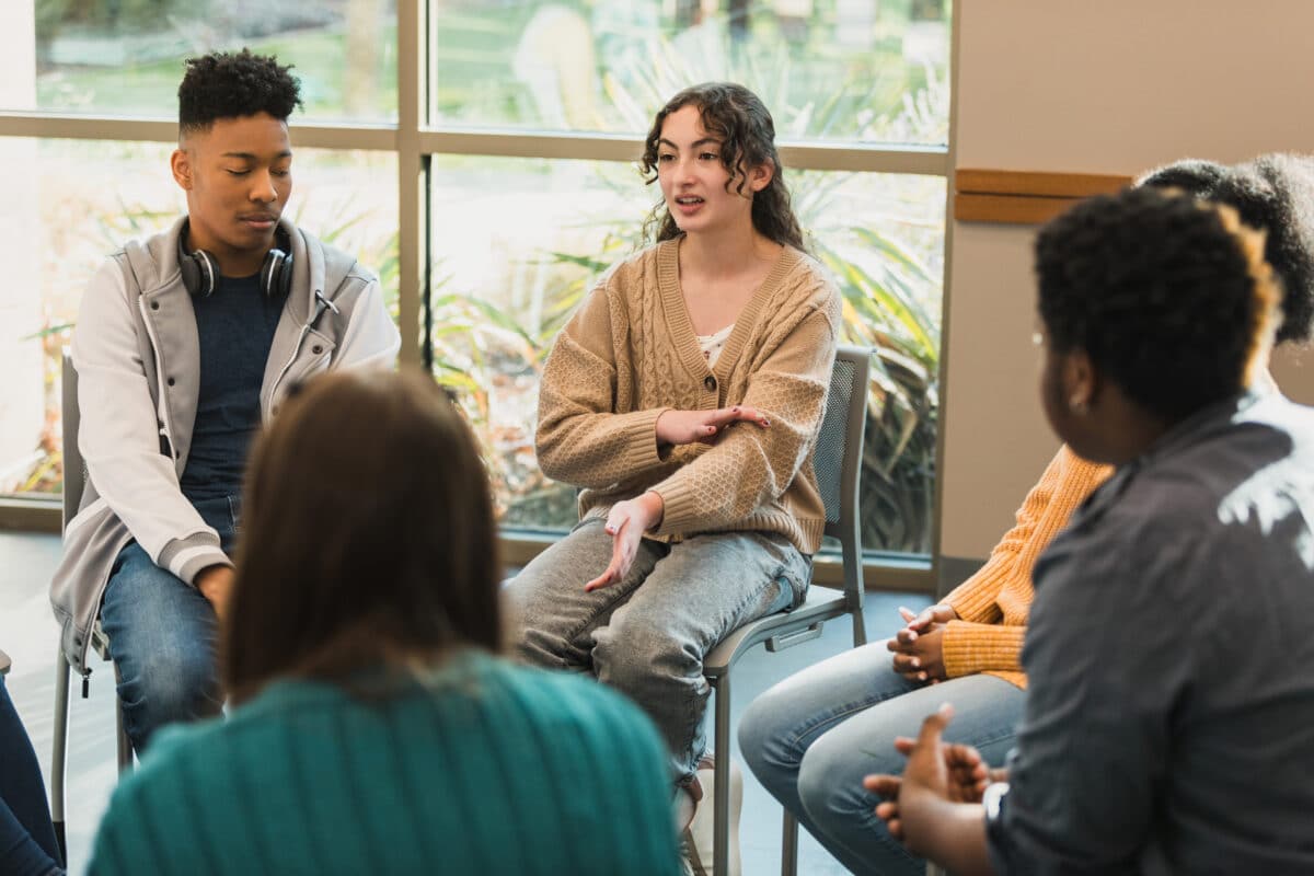 Young adults in a bright room taking part in a group discussion or therapy session.