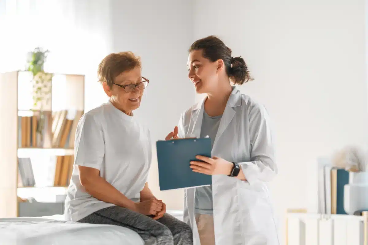 Healthcare professional discussing information on a clipboard with a patient in a clinic room.